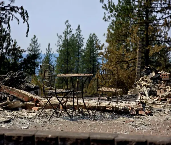 A wrought-iron bistro set standing on an undamaged brick patio. The house it belonged to is the rubble on either side.