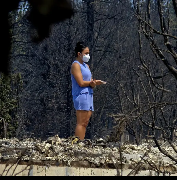 Standing on the foundation of a house, masked against the ash, looking at what is left of it.