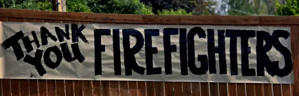 A hand-painted banner on a back fence, in a neighbourhood the fire stopped short of.